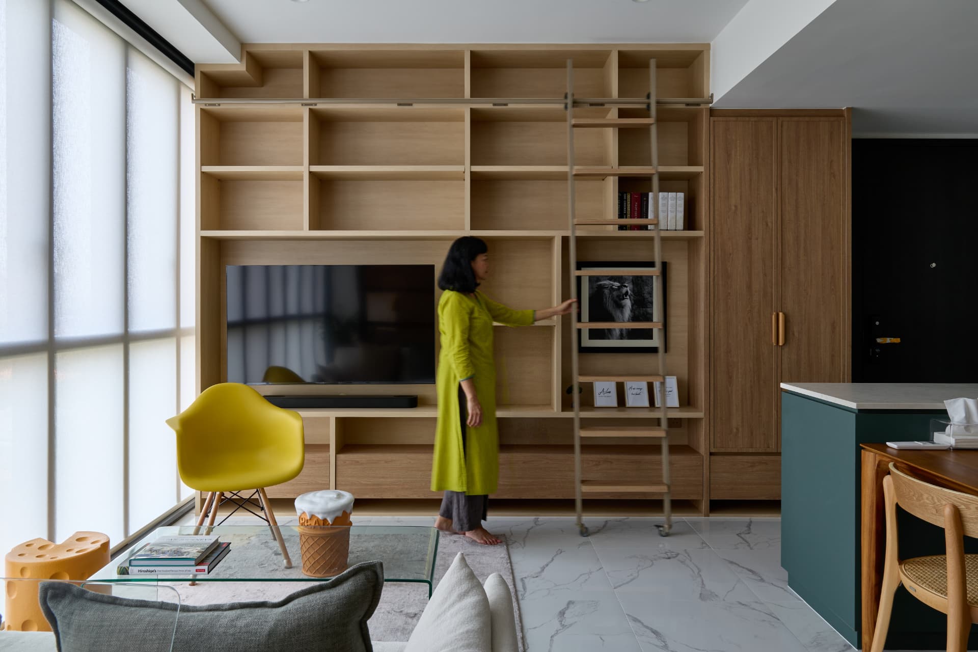 Living room with full-height timber shelving, a ladder and a yellow chair